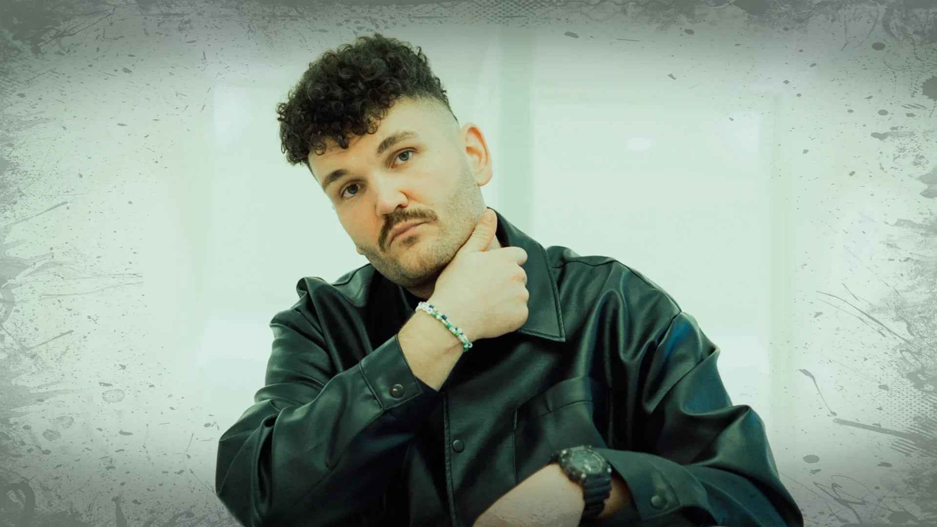 Man in black leather jacket posing with hand on neck, industrial techno style testimonial banner